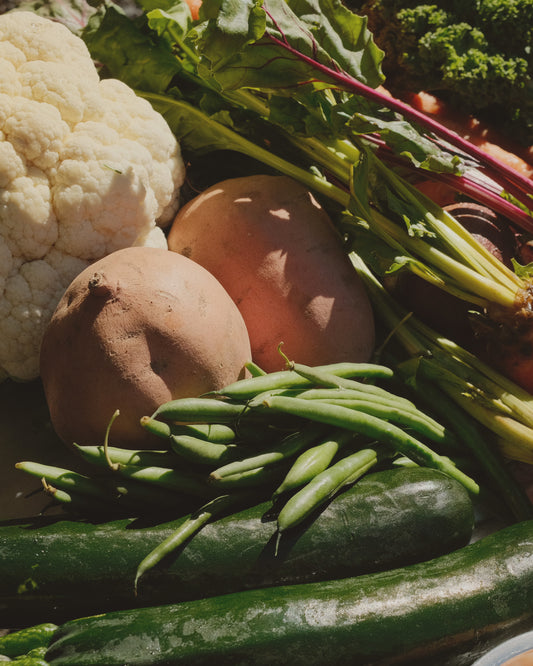 Assorted fresh vegetables including cauliflower, potatoes, green beans, and zucchinis on a dark background.
