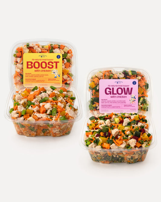 Two containers of dog meal topper with visible labels on a white background